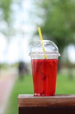 Tek kullanımlık plastik bardakta limonata, paket içecek. Yazın bir parkın arka planına karşı ferahlatıcı bir içecek. Ahududu ve limonlu pembe limonata. Tek kullanımlık bir bardakta içkinin yakın plan çekimi.