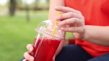 Tek kullanımlık bardakta limonata ile kadın ellerine yakın çekim. Yaz içeceği. Parlak tişörtlü kız parkta oturuyor. Yaz ve eğlence konsepti. Ahududu ve limonlu pembe limonata.