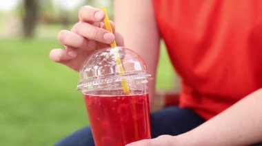 Tek kullanımlık bardakta limonata ile kadın ellerine yakın çekim. Yaz içeceği. Parlak tişörtlü kız parkta oturuyor. Yaz ve eğlence konsepti. Ahududu ve limonlu pembe limonata.