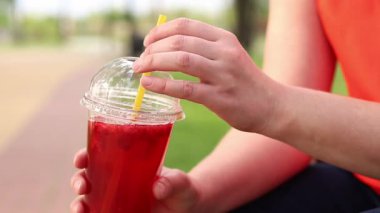 Tek kullanımlık bardakta limonata ile kadın ellerine yakın çekim. Yaz içeceği. Parlak tişörtlü kız parkta oturuyor. Yaz ve eğlence konsepti. Ahududu ve limonlu pembe limonata.