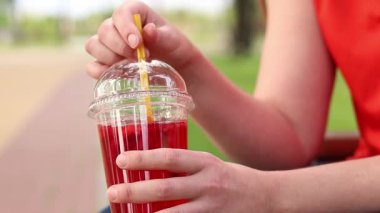 Tek kullanımlık bardakta limonata ile kadın ellerine yakın çekim. Yaz içeceği. Parlak tişörtlü kız parkta oturuyor. Yaz ve eğlence konsepti. Ahududu ve limonlu pembe limonata.