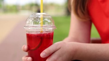 Tek kullanımlık bardakta limonata ile kadın ellerine yakın çekim. Yaz içeceği. Parlak tişörtlü kız parkta oturuyor. Yaz ve eğlence konsepti. Ahududu ve limonlu pembe limonata.