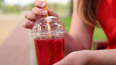 Tek kullanımlık bardakta limonata ile kadın ellerine yakın çekim. Yaz içeceği. Parlak tişörtlü kız parkta oturuyor. Yaz ve eğlence konsepti. Ahududu ve limonlu pembe limonata.