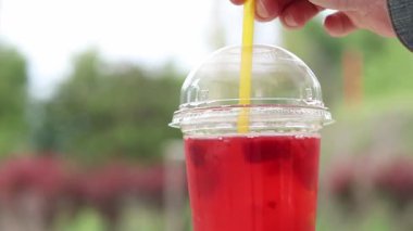 Tek kullanımlık plastik bardakta limonata, paket içecek. Yazın bir parkın arka planına karşı ferahlatıcı bir içecek. Ahududu ve limonlu pembe limonata. Tek kullanımlık bir bardakta içkinin yakın plan çekimi.