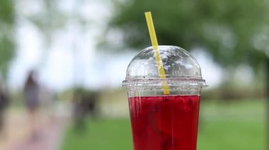 Tek kullanımlık plastik bardakta limonata, paket içecek. Yazın bir parkın arka planına karşı ferahlatıcı bir içecek. Ahududu ve limonlu pembe limonata. Tek kullanımlık bir bardakta içkinin yakın plan çekimi.