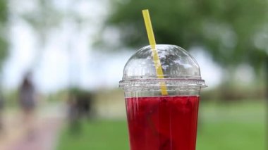 Tek kullanımlık plastik bardakta limonata, paket içecek. Yazın bir parkın arka planına karşı ferahlatıcı bir içecek. Ahududu ve limonlu pembe limonata. Tek kullanımlık bir bardakta içkinin yakın plan çekimi.