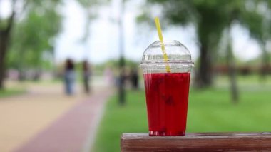 Tek kullanımlık plastik bardakta limonata, paket içecek. Yazın bir parkın arka planına karşı ferahlatıcı bir içecek. Ahududu ve limonlu pembe limonata. Tek kullanımlık bir bardakta içkinin yakın plan çekimi.