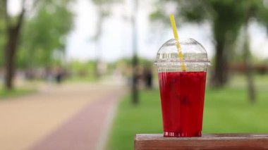 Tek kullanımlık plastik bardakta limonata, paket içecek. Yazın bir parkın arka planına karşı ferahlatıcı bir içecek. Ahududu ve limonlu pembe limonata. Tek kullanımlık bir bardakta içkinin yakın plan çekimi.