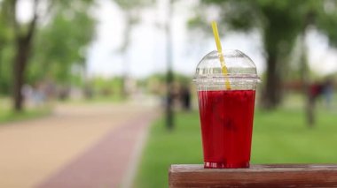 Tek kullanımlık plastik bardakta limonata, paket içecek. Yazın bir parkın arka planına karşı ferahlatıcı bir içecek. Ahududu ve limonlu pembe limonata. Tek kullanımlık bir bardakta içkinin yakın plan çekimi.