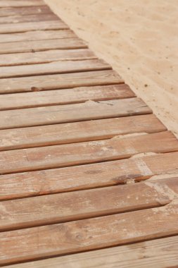 Sahilde tahta döşeme, tahtalara yakın çekim. Tahta kaldırım. Geçmişi. Yıpranmış ahşap tahtalar, dağınık kumlar, ılık yaz ışıkları. Seçici odak