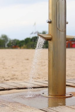 Plaj duşu, yakın çekim. Yaz tatili kavramı. Deniz ya da nehir kıyısında bir sahil duşu. Tatilcilerin rahatı için sahil bölgesinin düzenlenmesi. Ayakları kumdan temizlemek için duş