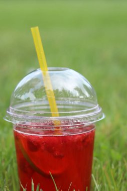 Tek kullanımlık plastik bardakta limonata çimlerin üzerinde duruyor. Yazın parkta serinletici bir içki. Ahududu ve limonlu pembe limonata. İçkiyi çimenlikteki tek kullanımlık bardakta yakın plan çek.