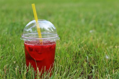 Tek kullanımlık plastik bardakta limonata çimlerin üzerinde duruyor. Yazın parkta serinletici bir içki. Ahududu ve limonlu pembe limonata. İçkiyi çimenlikteki tek kullanımlık bardakta yakın plan çek.