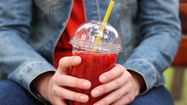 Elinde limonata olan kot ceketli bir kız, paket içecek. Yazın bir parkın arka planına karşı ferahlatıcı bir içecek. Tek kullanımlık bardakta içkiyle kadın ellerine yakın çekim. Yaz