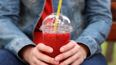 Elinde limonata olan kot ceketli bir kız, paket içecek. Yazın bir parkın arka planına karşı ferahlatıcı bir içecek. Tek kullanımlık bardakta içkiyle kadın ellerine yakın çekim. Yaz