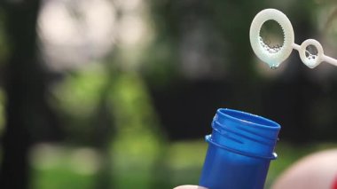 Sabun köpükleri. Parkta sabun köpüğü üflemek. Dışarıda sabun köpüğü şişiren bir kadın, yakın plan. Yaz tatili konsepti, huzurlu atmosfer. Tanınmayan kişi sabun köpüğü üflüyor.