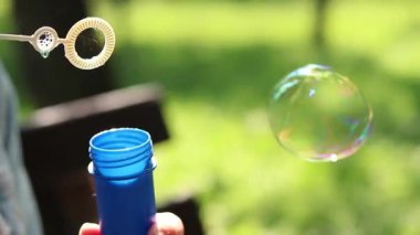 Parkta sabun köpüğü üflemek. Açık havada sabun köpüğü üfleme, yakın plan. Yaz tatili konsepti, huzurlu atmosfer. Tanınmayan kişi sabun köpüğü üflüyor. Açık hava eğlencesi. Boş zaman