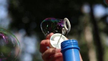 Parkta sabun köpüğü üflemek. Açık havada sabun köpüğü üfleme, yakın plan. Yaz tatili konsepti, huzurlu atmosfer. Tanınmayan kişi sabun köpüğü üflüyor. Açık hava eğlencesi. Boş zaman