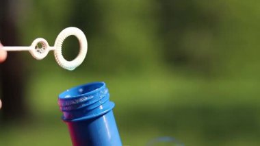 Parkta sabun köpüğü üflemek. Açık havada sabun köpüğü üfleme, yakın plan. Yaz tatili konsepti, huzurlu atmosfer. Tanınmayan kişi sabun köpüğü üflüyor. Açık hava eğlencesi. Boş zaman