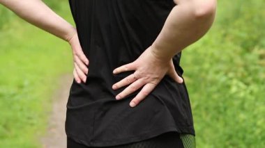 Antrenman sırasında sırt ağrısı sorunu. Spor kıyafetli bir kız sırtına masaj yapıyor. Ormandaki egzersizler. Sporcu olası bir spor sakatlığından sonra onu geride tutuyor. Belden aşağısı ağrıyor.