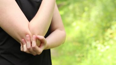 Antrenman sırasında dirsek sorunu. Spor kıyafetli kız yaralı koluna masaj yapıyor. Ormandaki egzersizler. Sporcu olası bir spor sakatlığından sonra elini tutuyor. Dirsek ağrısı.