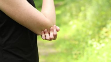 Antrenman sırasında dirsek sorunu. Spor kıyafetli kız yaralı koluna masaj yapıyor. Ormandaki egzersizler. Sporcu olası bir spor sakatlığından sonra elini tutuyor. Dirsek ağrısı.