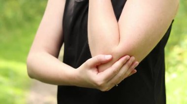 Antrenman sırasında dirsek sorunu. Spor kıyafetli kız yaralı koluna masaj yapıyor. Ormandaki egzersizler. Sporcu olası bir spor sakatlığından sonra elini tutuyor. Dirsek ağrısı.