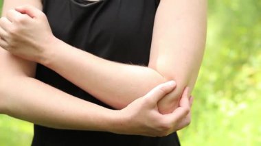 Antrenman sırasında dirsek sorunu. Spor kıyafetli kız yaralı koluna masaj yapıyor. Ormandaki egzersizler. Sporcu olası bir spor sakatlığından sonra elini tutuyor. Dirsek ağrısı.