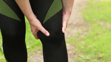 Antrenman sırasında diz sorunu. Spor kıyafetli kız yaralı bacağına masaj yapıyor. Ormanda koşuyor. Sporcu kadın olası bir spor sakatlığından sonra dizini tutuyor. Acı verici hisler ya da spazm