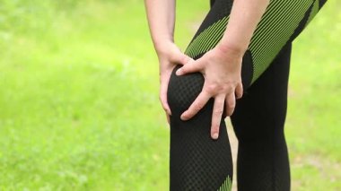 Antrenman sırasında diz sorunu. Spor kıyafetli kız yaralı bacağına masaj yapıyor. Ormanda koşuyor. Sporcu kadın olası bir spor sakatlığından sonra dizini tutuyor. Acı verici hisler ya da spazm