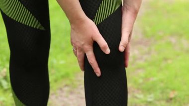 Antrenman sırasında diz sorunu. Spor kıyafetli kız yaralı bacağına masaj yapıyor. Ormanda koşuyor. Sporcu kadın olası bir spor sakatlığından sonra dizini tutuyor. Acı verici hisler ya da spazm