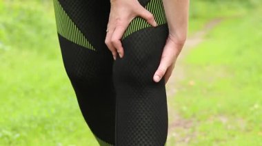 Antrenman sırasında diz sorunu. Spor kıyafetli kız yaralı bacağına masaj yapıyor. Ormanda koşuyor. Ani diz ağrısı. Açık hava eğitimi sırasında acı verici duygular. Kasılma ya da rahatsızlık