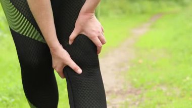 Antrenman sırasında diz sorunu. Spor kıyafetli kız yaralı bacağına masaj yapıyor. Ormanda koşuyor. Ani diz ağrısı. Açık hava eğitimi sırasında acı verici duygular. Kasılma ya da rahatsızlık