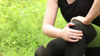 Antrenman sırasında diz sorunu. Spor kıyafetli kız yaralı bacağına masaj yapıyor. Ormanda koşuyor. Sporcu kadın olası bir spor sakatlığından sonra dizini tutuyor. Acı verici hisler ya da spazm