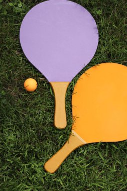 Plaj tenis raketleri ve top çimlerin üzerinde, üst manzara. Aktif yaşam tarzı, oyunlar ve spor. Plaj tenis takımı. Açık hava oyunları için parlak ahşap raketler. Yaz açık hava oyunları. Yaz sporları ve oyunlar konsepti