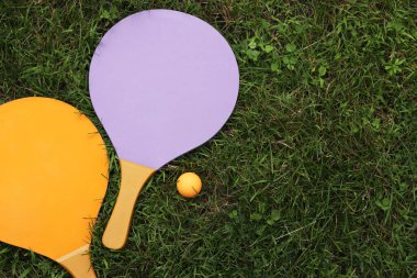 Plaj tenis raketleri ve top çimlerin üzerinde, üst manzara. Aktif yaşam tarzı, oyunlar ve spor. Plaj tenis takımı. Açık hava oyunları için parlak ahşap raketler. Yaz açık hava oyunları. Yaz sporları ve oyunlar konsepti