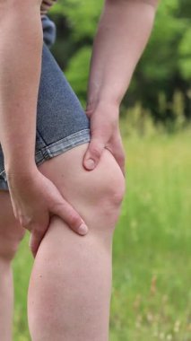 Swelling, cramping or pain in the legs. Girl massaging her leg, knee pain or cramp. Uncomfortable sensations during a walk. Woman stretching her leg against the backdrop of nature