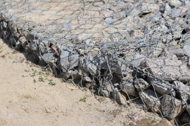 Gabion şilte, yol yaratmak için taşlardan örülmüş. Ağdaki taşlar, yollar açıyor, güçleniyor. Galvanize olmuş bir ağda yıkıntı ya da ezilmiş taş. Parktaki tamirat.