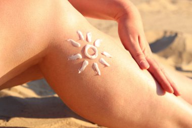 Bir kadının bacağında güneş kremi. Güneş kreminden yapılmış güneş kremi. Yaz mevsimi, sahil, güneş banyosu. Kumsalda güneşlenen bir kadın. Krem cildi güneşten, bronzlaşmadan ve korumadan korur.