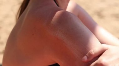 Cildine güneş kremi süren bir kadın. Yaz, sahil, bronzlaşma. Plajda mayo giyen bir kadın. Krem cildi güneş yanığından, bronzlaşmadan ve kremden korur. Plajda yaz tatili