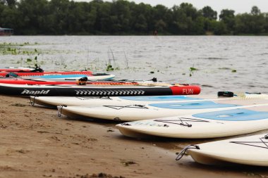 Kyiv, Ukrayna - 29 Temmuz 2025: Suda yüzmek için SUP tahtaları nehir kıyısında uzanır. Yazın aktif bir eğlence. Seyahat güzergahı, hobi ve su sporları için arazi aracı kiralama. Rüzgarlı hava