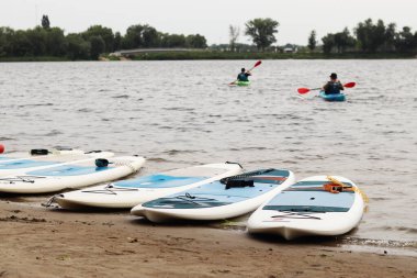 Kyiv, Ukrayna - 29 Temmuz 2025: Suda yüzmek için SUP tahtaları nehir kıyısında uzanır. Yazın aktif bir eğlence. Seyahat güzergahı, hobi ve su sporları için arazi aracı kiralama. Rüzgarlı hava