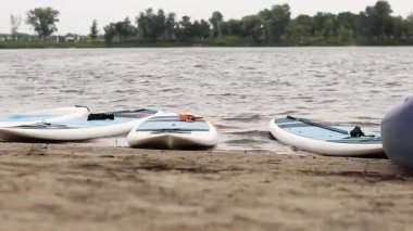 Kyiv, Ukrayna - 29 Temmuz 2025: Suda yüzmek için SUP tahtaları nehir kıyısında uzanır. Yazın aktif bir eğlence. Seyahat güzergahı, hobi ve su sporları için arazi aracı kiralama. Rüzgarlı hava
