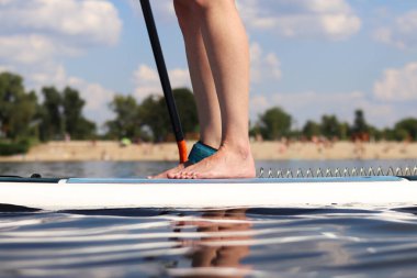 Ayakta duran bir kürek tahtası üzerinde duran kadın bacaklarının yakın çekimi. Stand-up 'a binen bir kız. Aktif yaz tatili. Su sporları. Nehirde yüzen küreklerle ayakta duran bir kız.