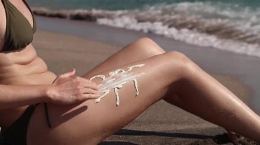 Güneş kremiyle yapılmış bir kadının bacağında SPF yazılıydı. Cilde güneş kremi sürmeye yakın çekim. SPF koruması. Plaj tatili Güvenli bronzlaşma. Deniz tatili, kumsalda güneşlenme.