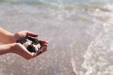 Bir avuç kabuk ve deniz kumu tutan kadın ellerinin yakın çekimi. Denizde tatil, deniz kenarında tatil. Elinde deniz kabukları tutan bir kız. Eller deniz dalgalarının arka planında. Plaj