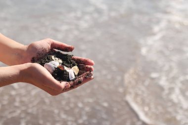 Bir avuç kabuk ve deniz kumu tutan kadın ellerinin yakın çekimi. Denizde tatil, deniz kenarında tatil. Elinde deniz kabukları tutan bir kız. Eller deniz dalgalarının arka planında. Plaj