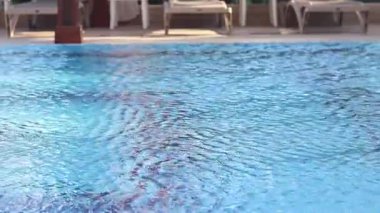Havuzda suyun yüzeyinde küçük dalgalanmalar var. Suyun altında mavi fayanslı yüzme havuzu. Tatil teması. Arka plan olarak kullanılmak üzere su yüzeyinin videosu. Turizm kavramı, tatil