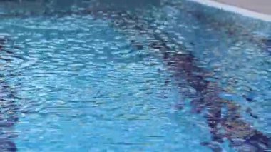 Havuzda suyun yüzeyinde küçük dalgalanmalar var. Suyun altında mavi fayanslı yüzme havuzu. Tatil teması. Arka plan olarak kullanılmak üzere su yüzeyinin videosu. Turizm kavramı, tatil