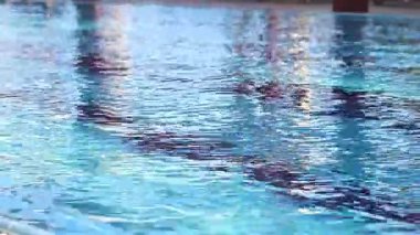Havuzda suyun yüzeyinde küçük dalgalanmalar var. Suyun altında mavi fayanslı yüzme havuzu. Tatil teması. Arka plan olarak kullanılmak üzere su yüzeyinin videosu. Turizm kavramı, tatil